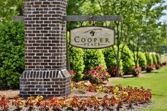 the sign for cooper place is surrounded by flowers and shrubs in front of a brick pillar