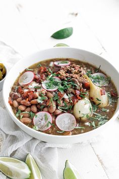 a white bowl filled with beans, meat and veggies on top of a table