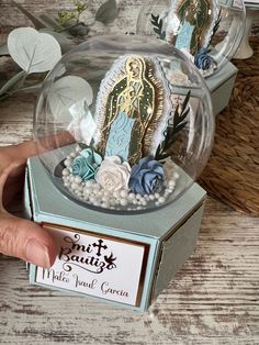 a hand is holding a glass ball with an image of the virgin mary in it