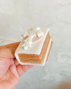 a hand holding a piece of cake with icing on it's top and bottom