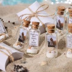 small glass bottles filled with sand and seashells are on the beach next to a gift box