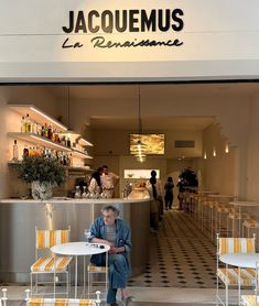 a woman sitting at a table in front of a restaurant with yellow and white striped chairs