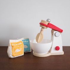 a wooden toy mixer sitting on top of a table next to a bag of flour