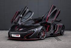 a black and red sports car parked in front of a gray wall with its doors open