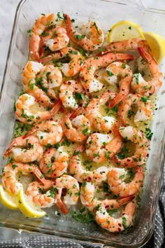 a glass casserole dish filled with shrimp and garnished with lemon wedges