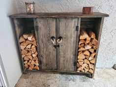 a wooden cabinet filled with firewood stacked on top of each other next to a wall