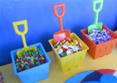 a table topped with plastic containers filled with candies and pineapples next to a blue wall