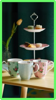 three cups on a table with two trays holding donuts and one teacup