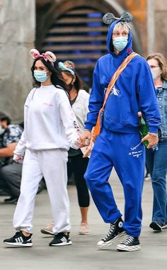 two people wearing face masks walk down the street with other people in front of them