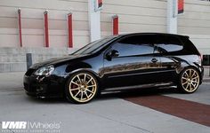 a black car parked in front of a building with gold rims on it's wheels