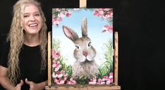 a woman standing next to an easel with a painting on it's side