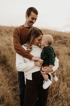 a man and woman holding a baby in their arms while standing in a field with tall grass