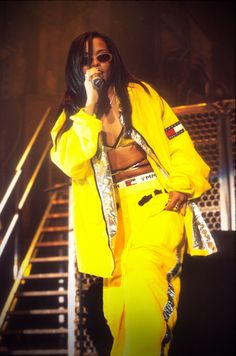 a woman in yellow outfit holding a microphone and singing into a microphone while standing next to stairs