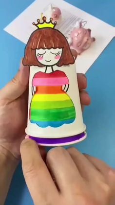 a hand holding a small cup with a girl on it and a rainbow painted inside