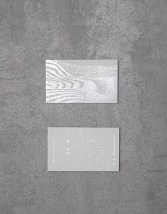 two business cards sitting on top of a gray surface next to each other with white writing