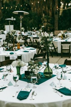 a table set up for an outdoor wedding with green napkins and white flowers in vases