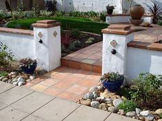 two planters are on the side of a white wall near some rocks and plants