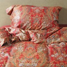 an orange and red bed spread on top of a wooden headboard next to a wall