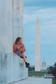 a woman sitting on the side of a wall next to a large monument with a washington monument in the background