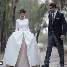 a man and woman walking down a dirt road in wedding gowns with long sleeves