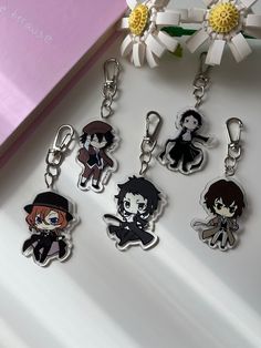 four keychains with anime characters on them sitting next to a pink box and flower