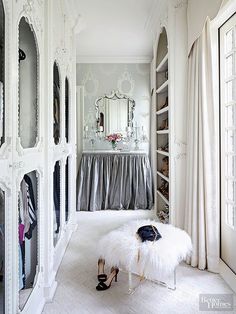 the closet is decorated in white and has a bench with fur on it, along with several pairs of shoes