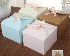 four different colored boxes with bows on them sitting on a wooden table next to flowers