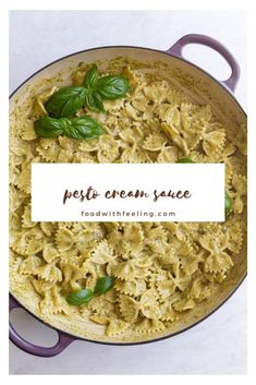 pasta with pesto cream sauce and basil leaves in a purple pan on a white surface