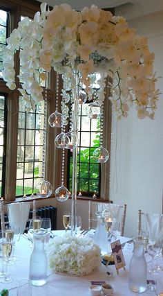 a tall centerpiece with white flowers and crystal balls is displayed on a table in front of windows