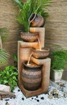 an outdoor fountain with three pots and water pouring out of it's sides, surrounded by plants