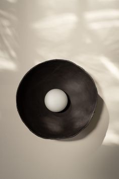 a black bowl with an egg in it on a white tableclothed surface, casting a shadow