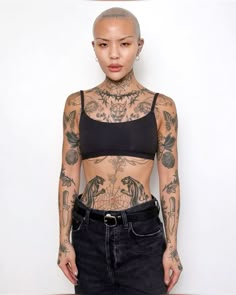 a woman with tattoos on her chest and arms standing in front of a white wall