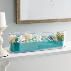 a glass container filled with sea shells on top of a white table next to a candle