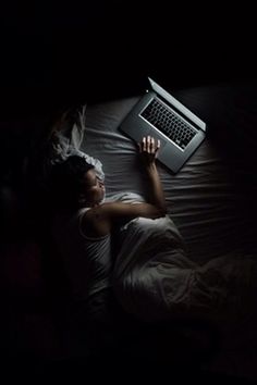 a person laying in bed with a laptop on their lap and head turned to the side