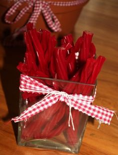 a glass vase filled with red candy canes on top of a wooden table next to a potted plant