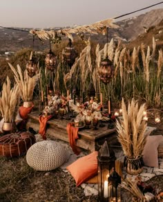 an outdoor setting with candles, pillows and other items on the ground in front of some tall grass