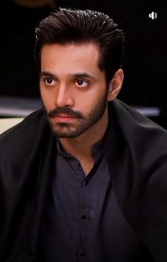 a man with a goatee and black shirt looking at the camera while sitting down