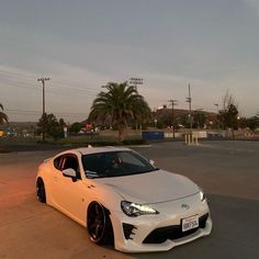 a white sports car parked in a parking lot next to some palm trees and buildings