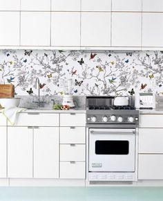 a kitchen with white cabinets and a silver stove top oven in front of a wallpapered backsplash