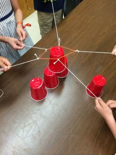 some red cups are on a table and one is connected to the other with string