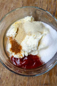 ingredients in a glass bowl on top of a wooden table, including cream cheese and ketchup