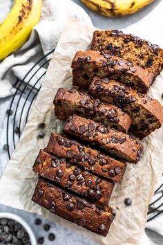 slices of chocolate chip banana bread on a wire rack with two bananas in the background