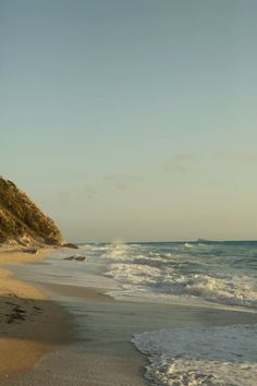 a sandy beach next to the ocean with waves coming in on it's shore