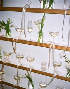 there are many wine glasses with flowers in them on the shelf next to each other