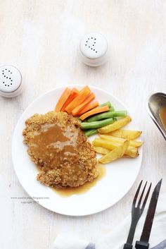 a white plate topped with meat covered in gravy next to fries and carrots