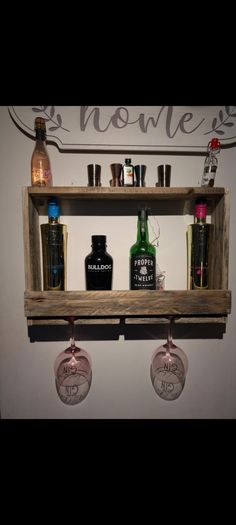 two wine glasses are sitting on a shelf with liquor bottles and shot glasses hanging from it