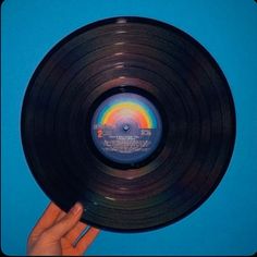 a hand holding up a black record on a blue background with the rainbow in it