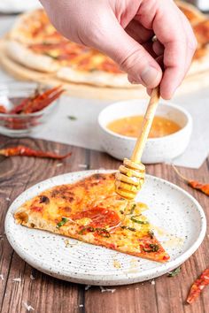 a slice of pizza on a plate being held by a wooden stick with dipping sauce