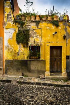 an old yellow building with potted plants on it