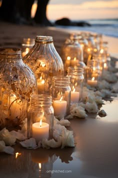 candles are lined up on the beach near vases